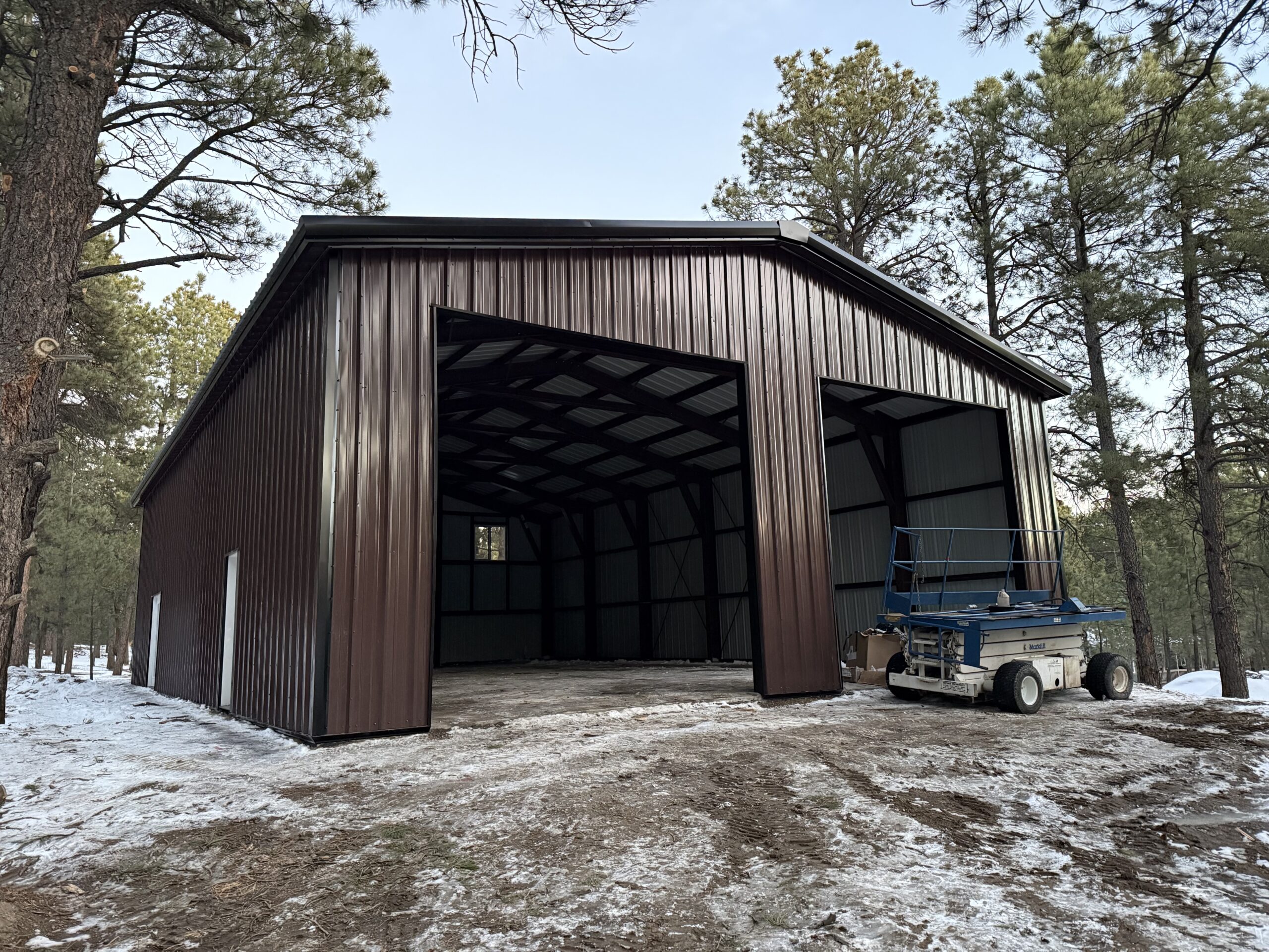 Finished brown steel building with two overhead door bays in the Black Forest pines
